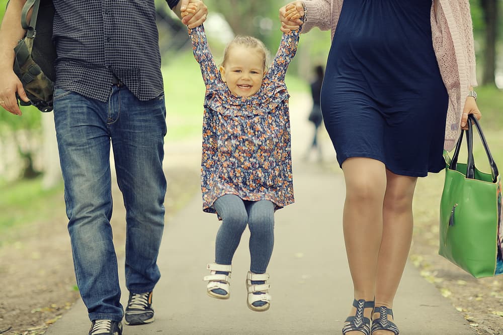 Parents happily lifting their daughter by the hands while walking outdoors