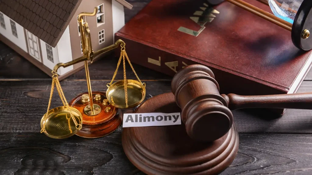 A gavel, scales of justice, a law book, and a small house model with the word "Alimony," symbolizing legal proceedings related to spousal support.