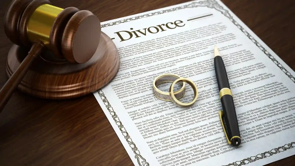 Divorce papers with a gavel, wedding rings, and pen on the table.
