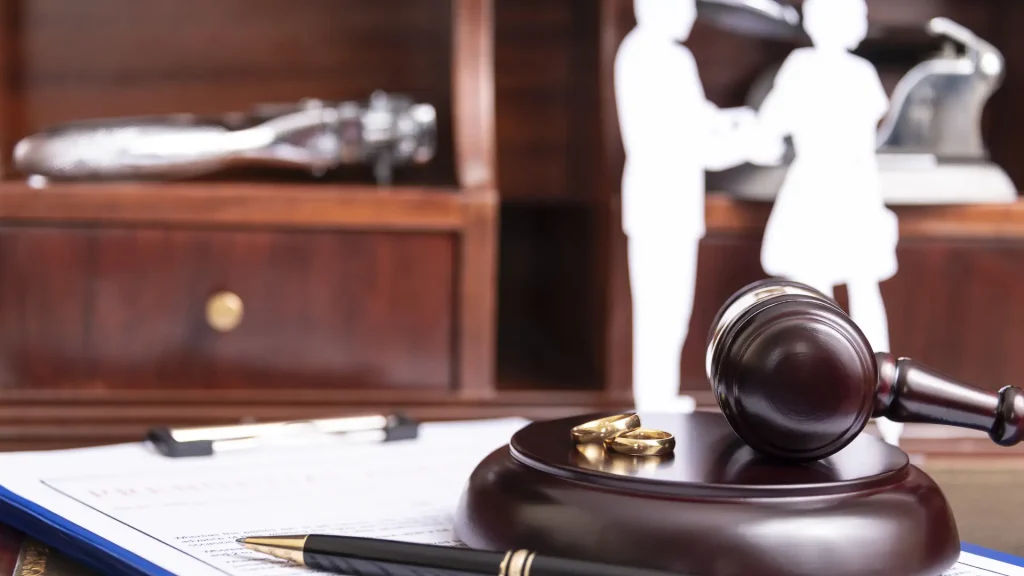 Close-up of a gavel, pen, and wedding ring on a desk with legal figurines in the background