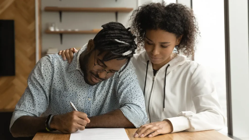Couple signing documents together with one person offering support