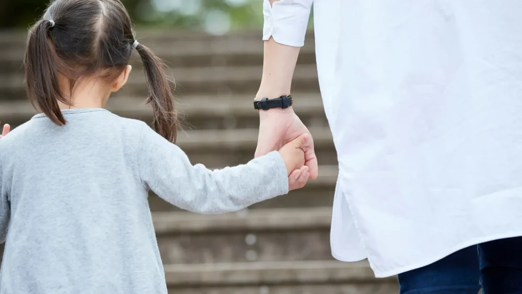 A close-up of a child holding an adult's hand while walking, symbolizing care and guidance.