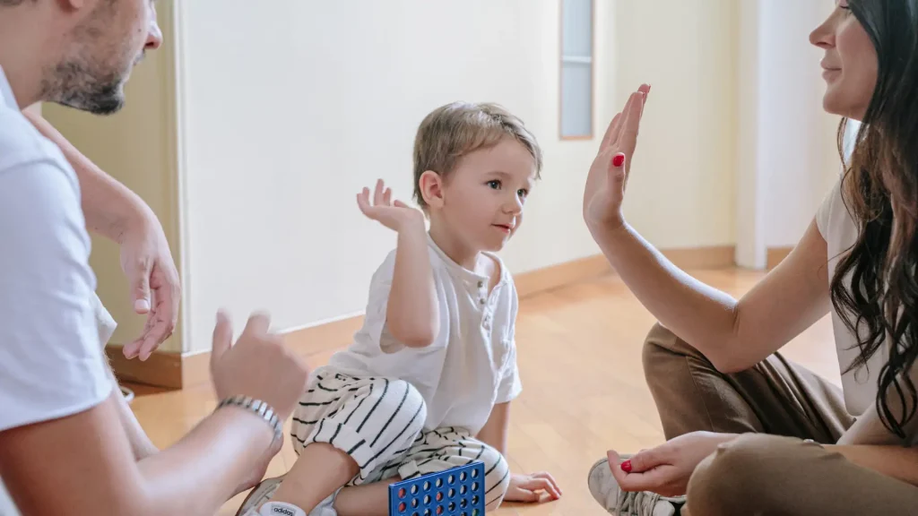 A young child giving a high-five as part of a playful interaction with others.
